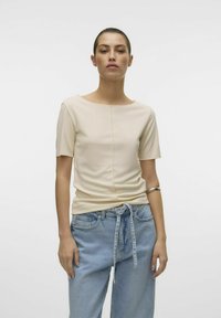 Beige tætsiddende top med korte ærmer, der har en rund halsudskæring og centralt sømdetalje, parret med lyseblå løse denimjeans.