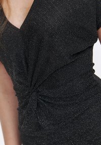 Czarna sukienka z głębokim dekoltem w kształcie litery V, z twisting knot w talii i fakturowaną powierzchnią ozdobioną srebrnymi plamkami.