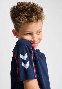 Marinblått idrottströja med röda accenter, prydd med vita chevronmönster på ärmarna, tillverkad av mjukt och lätt tyg.