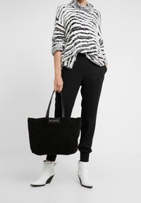 Svart fodrad tote-väska med svarta handtag, ihopparad med en vit och svart randig, fluffig tröja, svarta byxor och vita klackiga ankelboots.