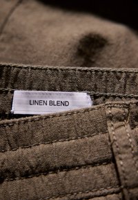 Linneblandningstyg i brun med en strukturerad yta. Har en vit etikett med texten "LINNEBLANDNING" sydd i sömmen.