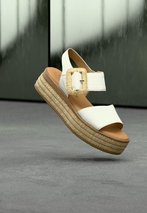 Witte plateausandalen met een geweven gespsluiting, leren banden, een espadrille-achtige geweven zool en een lichtbruine voetbed.