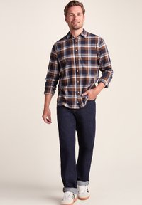 Checkered flannel shirt in navy, orange, and white; long sleeves with button cuffs, paired with dark denim jeans and white sneakers.
