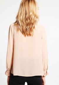 Vaaleanpunainen paita pitkähihaisilla hihoilla, jossa on pleatatut hihansuut, löysä istuvuus ja sileä, kevyt kangas. Takakatsaus näkyvissä.