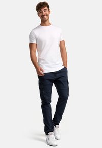 Valkoinen lyhythihainen t-paita, tummansiniset cargo-housut taskuilla ja valkoiset lenkkarit. Rentoa istuvuutta, pehmeä pinta ja yksinkertainen muotoilu.