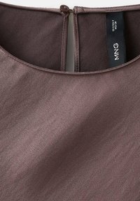 Encolure d'un chemisier en satin mauve foncé avec un petit bouton marron et une étiquette noire indiquant la taille et la marque.