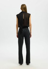 Blouse noire plissée sans manches avec un nœud à l'arrière, associée à un jean en denim foncé taille haute et taille ajustée. Texture lisse, léger éclat.