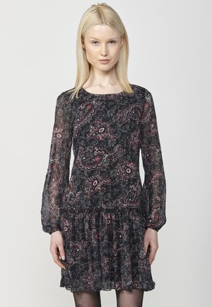 Robe noire à manches longues ornée d'un motif paisley en rouge et blanc, avec une taille froncée et un ourlet volanté. Fabriquée en tissu léger.