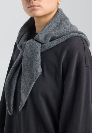 Persoon draagt een zwarte top met een zachte, dikke grijze sjaal die losjes om de nek is geknoopt en over de schouders is gedrapeerd.