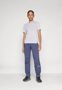 Φωτεινό μωβ κοντομάνικο πουκάμισο με λευκό λογότυπο, συνδυασμένο με σκούρο μπλε παντελόνι με λογότυπο στο πλάι. Μαύρα αθλητικά παπούτσια ολοκληρώνουν την εμφάνιση.