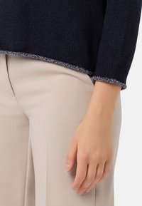 Maglione a maglia blu navy con finitura testurizzata e orlo con accenti argentati, abbinato a pantaloni in tessuto liscio di colore crema.