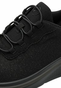 Must mustsneaker, millel elastsete nööpide süsteemiga, tekstuuritud ülemine osa ja sile kummist tald, millel on mustriline haardepind. Minimalistlikud disainelemendid.
