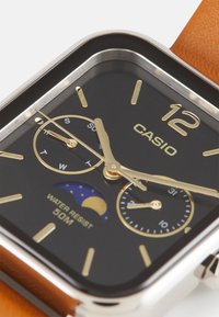 Montre Casio avec un cadran rectangulaire noir, des accents dorés, un bracelet en cuir marron, un affichage de phase de lune et une résistance à l'eau jusqu'à 50 mètres.