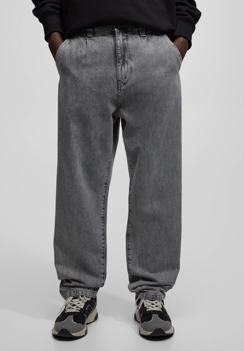 Grå denimbyxor med lös passform, hög midja, sidofickor och subtilt blekning. Matchas med svarta och grå sneakers.