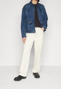 Jeansjacka i mörkblå med flera fickor, matchad med krämfärgade byxor med vida ben och svarta stövlar med texturerade sulor.