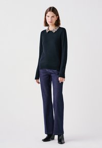 Maglione nero con colletto a stampa leopardata, abbinato a jeans a zampa d'elefante blu scuro e stivaletti neri con tacco. Tessuto morbido e design aderente.