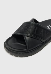 Chinelos de slide pretos com uma tira texturizada com letras em relevo, um cabedal sintético liso e uma sola de borracha flexível.