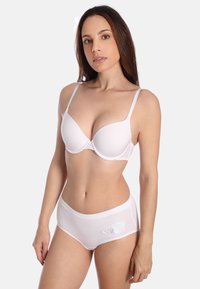 Witte lingerie set bestaande uit een gevoerde beha met verstelbare bandjes en bijpassende hoge slip, textuurstof en bloemige borduurdetails.