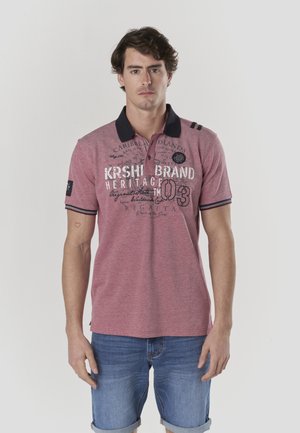 Polo rojo de manga corta con cuello azul marino y puños a rayas. Presenta un estampado gráfico en la parte delantera y un detalle en el hombro. Combina con pantalones cortos de mezclilla.