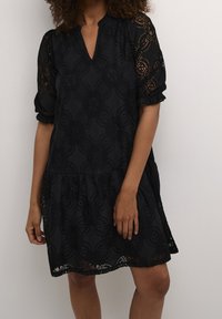 Svart spetsklänning med V-ringning och korta puffärmar. Designen inkluderar blommönster och en lager-på-lager kjol. Delikat textur.