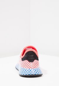 Baskets en maille blanches avec des accents rouges et bleus, dotées d'un talon en suède noir et d'un motif de grille texturé sur la semelle.