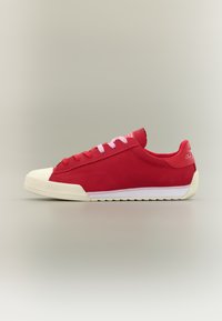 Κόκκινο αθλητικό παπούτσι χαμηλού προφίλ με λευκή λαστιχένια σόλα και μύτη, με ροζ και κόκκινα κορδόνια, απεικονίζεται σε ουδέτερο φόντο και στρέφεται προς τα αριστερά.