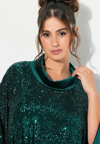 Teal, glitrende top med en glat satin krave. Har en løs pasform og teksturerede detaljer skabt af reflekterende paletter.
