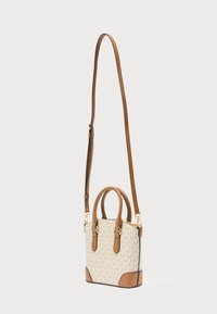 Petit sac à main avec un corps en tissu crème présentant un motif de logo répété, des accents en cuir marron et une bandoulière amovible.