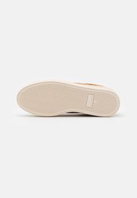 Suela de zapato con un patrón de espiga, material de goma de color beige claro y una etiqueta de logo prominente. El diseño es plano y circular en la puntera.