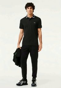 Zwarte poloshirt met een contrasterende gestreepte kraag, gecombineerd met zwarte broek. Opvallend logo detail op de borst en sportieve zwarte schoenen.