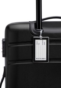 Zwarte harde koffer met een getextureerd oppervlak, uitschuifbare handgreep en een baggage-label met contactvelden. Voorzien van ritsen en een stevige constructie.