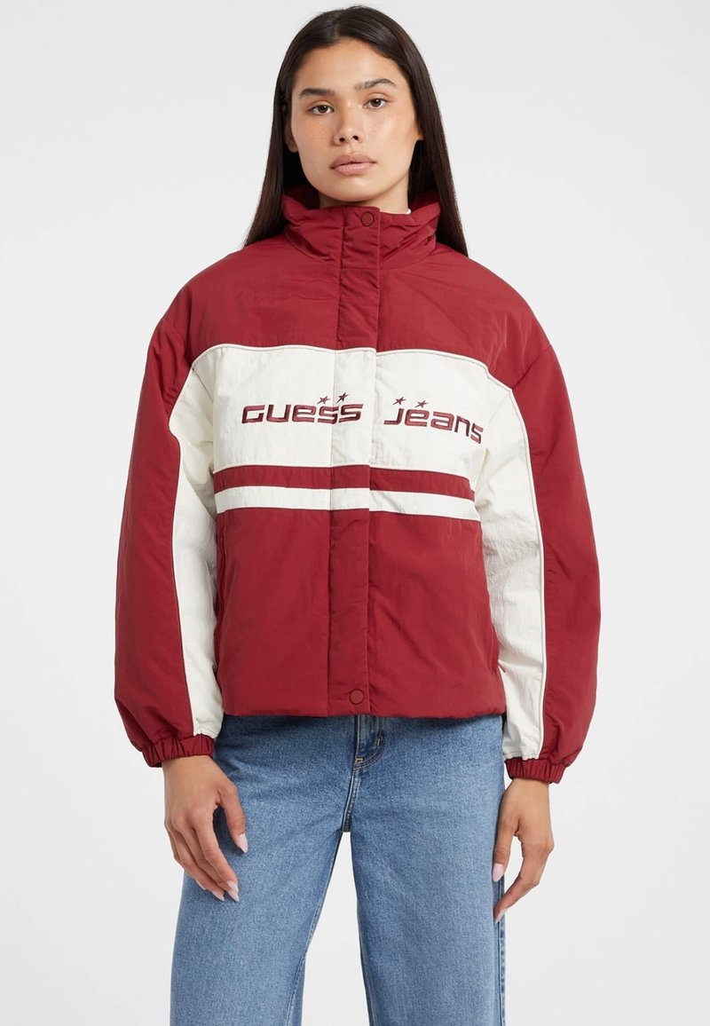 Rød og hvid quilted jakke med høj krave, med "Guess Jeans" logo og elastiske manchetter, parret med blå denim jeans.