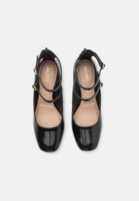 Paire de chaussures Mary Jane noires en cuir verni avec double bride cheville et semelles beige marquées "ALDO", vues de dessus sur fond blanc.