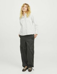 Camisa blanca de botones con un ajuste entallado, combinada con pantalones cargo sueltos de color gris oscuro que tienen bolsillos laterales y zapatillas de malla negras tipo slip-on.