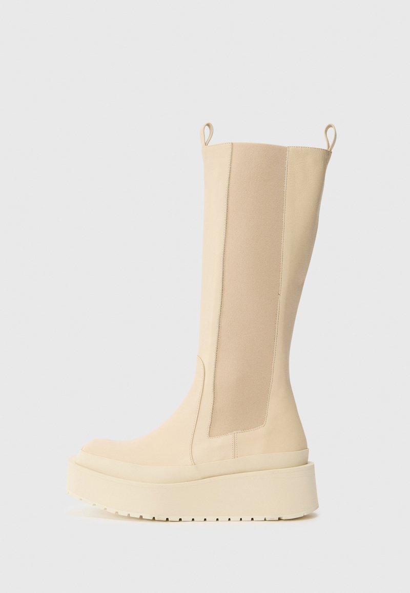 Botas beiges hasta la rodilla con acabado mate, paneles laterales elásticos, punta redonda, suela de plataforma gruesa y lengüetas en la parte superior para facilitar su puesta.