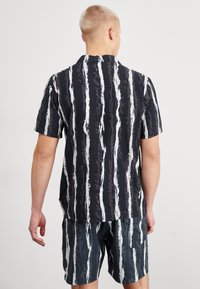 Camisa de manga corta de rayas verticales en blanco y negro con un corte relajado y cuello, combinada con pantalones cortos a juego que presentan un patrón similar.