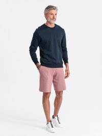 Marineblauwe sweatshirt met een ronde hals, gecombineerd met lichtroze textuurbroekjes. Witte sneakers met zwart en rode accenten.