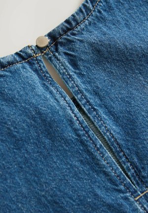 Denimplagg med en skön halsringning och metallknappstängning. Tyget har en blå tvätt med tydliga sömsdetaljer.