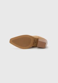 Pantofii din suede maron cu toc înalt și vârf ascuțit. Talpa are un cauciuc texturat pentru aderență. Toc bloc cu un finisaj neted și detalii cu logo embosat.