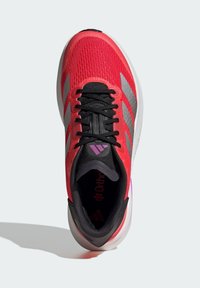 Red athletic shoe featuring a textured upper, black accents, grey stripe design, and a cushioned sole with pink detailing. Laced with flat black laces.
