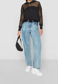 Sudadera de malla negra con cordones, combinada con unos vaqueros de pierna ancha azul claro. Zapatillas blancas y un bolso negro pequeño completan el look.