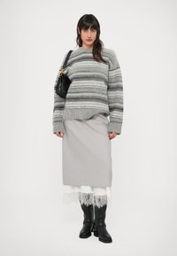 Gray striped sweater with a relaxed fit, paired with a light gray skirt featuring lace trim, and knee-high black boots. Black handbag.