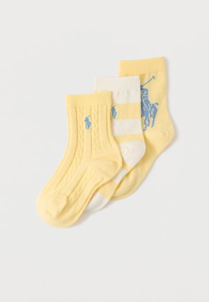 Tri zložene otroške nogavice v rumeni in beli barvi z modrimi logotipi igralcev polo, z enobarvnimi, črtastimi in pletenimi vzorci.