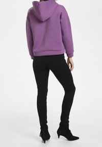 Sweat-shirt à capuche violet avec une coupe décontractée, associé à un legging noir et des bottines noires à franges. Texture lisse dans l'ensemble.