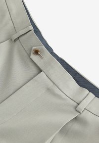 Hellgraue Hose mit glatter Textur, seitlichem Knopfverschluss und einem kontrastierenden dunkelblauen Bund. Die Nähte sind sichtbar.