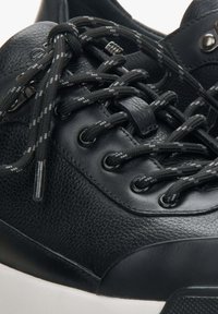 Czarne skórzane sneakersy z teksturowanym wierzchem, okrągłym noskiem oraz kontrastującymi czarno-szarymi sznurówkami w drobne plamki. Posiadają metalowe oczka oraz amortyzującą podeszwę.