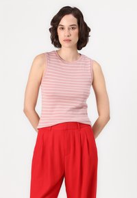 Top senza maniche a righe rosa realizzato in tessuto morbido, con scollatura rotonda. Abbinato a pantaloni rossi a vita alta, che mettono in risalto un taglio sartoriale.