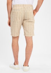 Beige striped shorts with an elastic waistband and two back pockets. Worn with white sneakers.
