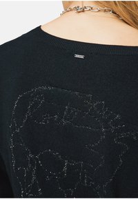 Maglione nero con un design grafico testurizzato e lucido sulla schiena. Scollo rotondo con bordo a coste, etichetta attaccata vicino al colletto.