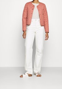 Giacca trapuntata corallo, camicia a righe, jeans bianchi a vita alta e sandali bianchi con suola in sughero. Design aderente con bottoni a pressione.